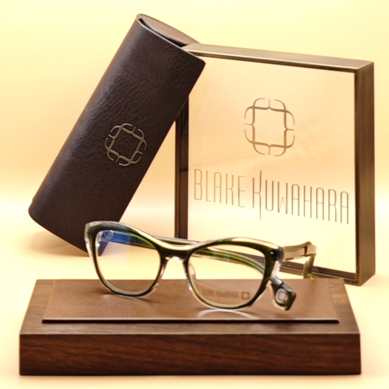 Blake Kuwahara's Bayer upswept cat-eye optical frame in dark forest green with bright green and yellow interior accents.