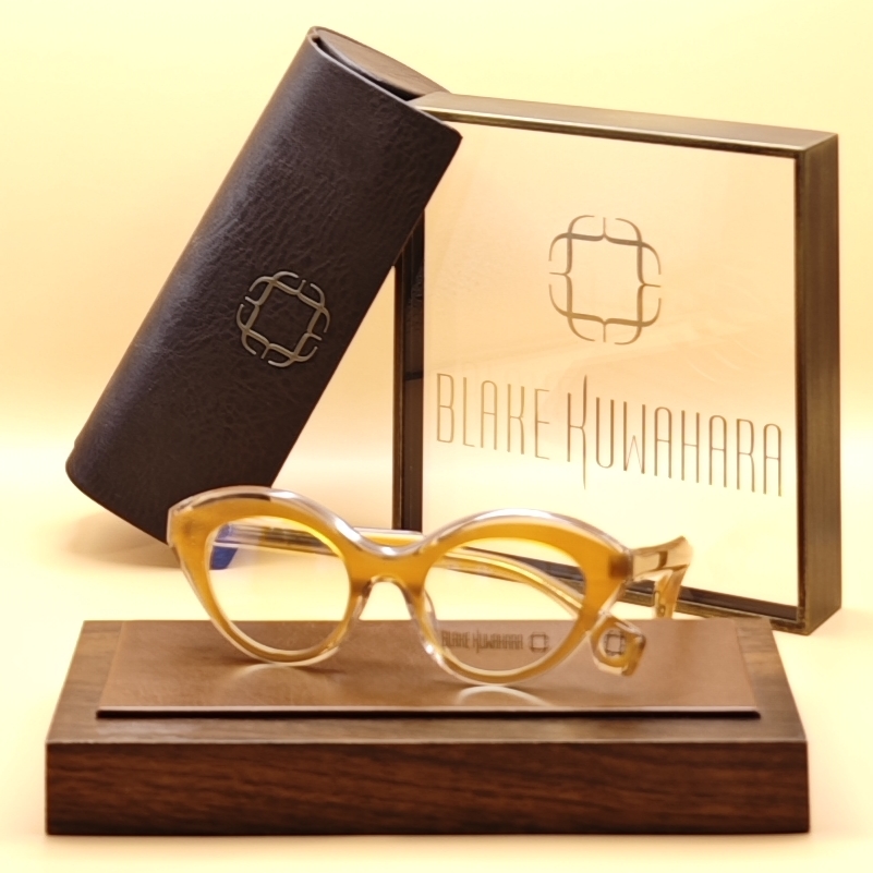 Blake Kuwahara 'Bullard' cat-eye glasses in a translucent, glossy amber/yellow acetate, displayed with the matching brown leather case and signature gold box.